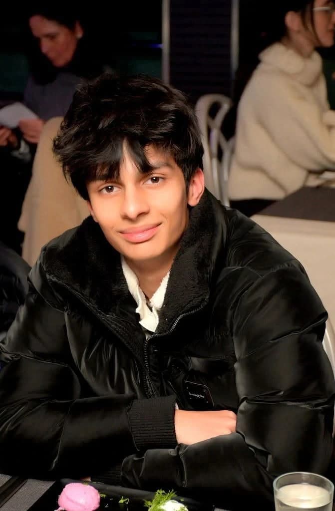 Devansh smiling at a dinner table, in a black puffer jacket