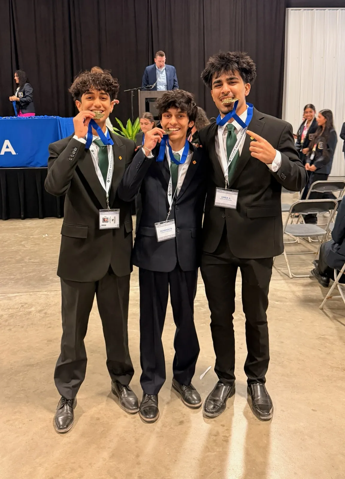 Devansh and two teammates in suits, showing their medals