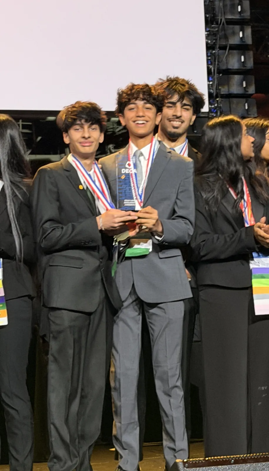 Devansh and teammates on stage holding a trophy, wearing medals