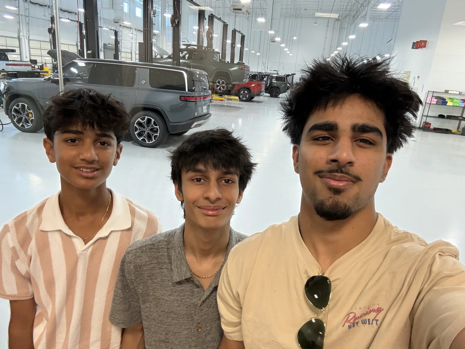 Selfie of three people inside a Rivian service bay, with an R1S behind them